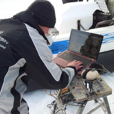 Nick crouched in the snow, tuning ECU calibration on a hovercraft from a laptop balanced on a workbench.